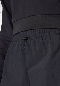 Svart atletisk topp och byxor; toppen har en tjock ribbad midja, byxorna har en elastisk midja med dragsko och en slät textur.