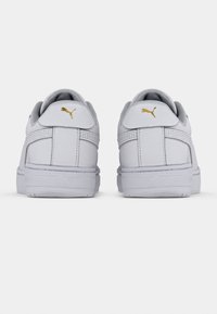 Vita sneakers med slätt läderöverdel, rund tå, vadderad krage och guld Puma-logotyp vid hälen. Platt gummisula, minimal design.