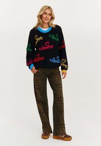 Czarny sweter robiony na drutach z kolorowym napisem "Amore" i wzorami serc; połączony z spodniami w leoparda o wysokim stanie i brązowym obuwiem.