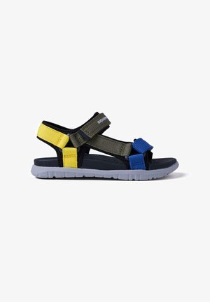 Sandalia infantil con base negra y tiras amarillas, verdes y azules. Cuenta con cierres ajustables de Velcro y suela de goma gris.