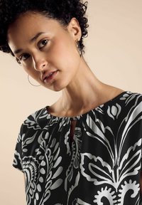 Blusa nera con motivi floreali bianchi, scollo rotondo con dettaglio a occhio di chiave, maniche corte e una texture di tessuto morbido.