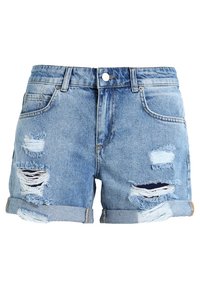 Shorts de denim en azul claro con bordes deshilachados, múltiples parches rasgados y dobladillos enrollados. Presentan un botón en la parte delantera y bolsillos.