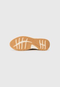Shoe sole with a rubber material, featuring a tan color, tread pattern, and a smooth white accent area for improved grip and traction.