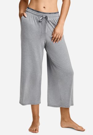 Woman wearing gray wide-leg cropped lounge pants with drawstring waist and elastic band branded Jockey, standing barefoot with one hand in pocket.