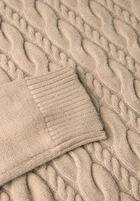 Maglione beige lavorato a maglia con motivo a trecce e polsini a costine, caratterizzato da una texture morbida e un design classico.