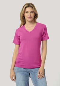 T-shirt à col en V en tissu lisse et léger de couleur rose vif. Manches courtes et silhouette ajustée. Associé à un jean en denim bleu clair.
