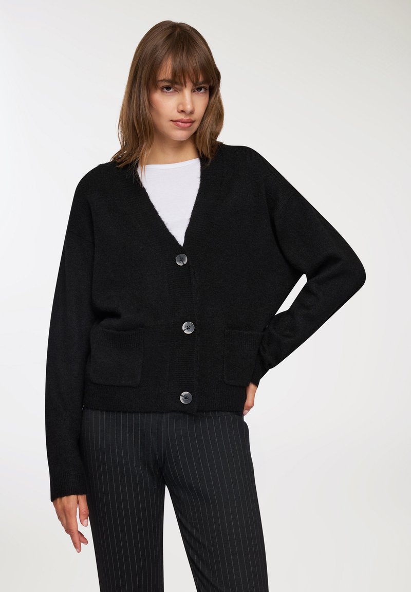 Cardigan nero a maglia con scollo a V, dotato di chiusura con bottoni e due tasche frontali. La texture è morbida, con una vestibilità comoda e maniche lunghe.