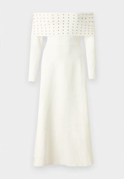 Witte off-the-shoulder jurk met lange mouwen, voorzien van een gestructureerd lijfje versierd met zilveren studs, een uitlopende zoom en gegolfde randen.