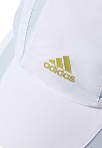 Biała czapka z jasnoniebieskimi akcentami, wykonana z teksturowanej tkaniny, z wyraźnym żółtym logo Adidas z przodu.