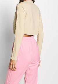 Beige långärmad cropped top med rund halsringning som matchar med rosa, mjuka, dra åt sweatpants med sidoplieringar.