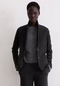 Black pinstripe jacket with notch lapels, gray knit sweater underneath, and tailored pants, featuring a soft texture and fitting silhouette.