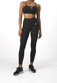 Czarny sportowy stanik i legginsy wysokiej talii, charakteryzujące się gładką fakturą i białymi akcentami logo. Uzupełnione czarnymi butami do biegania.