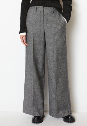 High-waisted, wide-leg gray herringbone trousers worn with black chunky shoes and a black ribbed sweater with white cuffs.