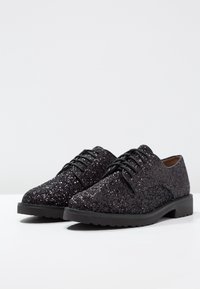 Chaussures Oxford à paillettes noires avec un bout arrondi et une semelle noire épaisse, dotées de lacets et d'une surface texturée. Pas de motifs ou accents remarquables.