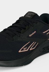 Μαύρο αθλητικό παπούτσι Reebok με ροζ λεπτομέρειες, επάνω μέρος από δίχτυ, κορδόνια και λογότυπα στη πλευρά και στη γλώσσα.