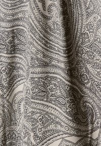Tissu à motifs présentant des motifs paisley complexes en noir sur un fond beige clair. Le matériau a une apparence douce et texturée.