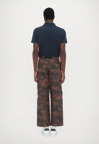 Marinblå pikétröja med korta ärmar i kombination med bruna camouflage-byxor med sidfickor och en avslappnad passform, bärs med vita sneakers.