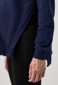 Marinblå sweatshirt med avslappnad passform, med rullade ärmslut och delad nederkant, kombinerad med svarta leggings. Slen yta, avslappnad design.