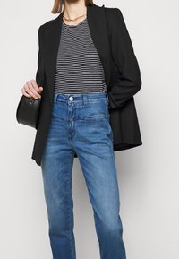 Svart blazer, randig t-shirt och blå denimjeans visas tillsammans. Blazern har en strukturerad design; jeansen har en åtsittande midja och klassisk passform.