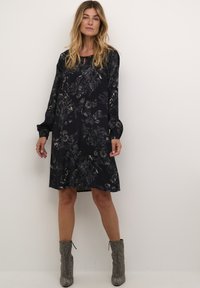 Langärmliges schwarzes Kleid mit floralem Muster, lässige Passform, knielanger Saum, weicher Stoff. Kombiniert mit metallischen Ankle Boots.