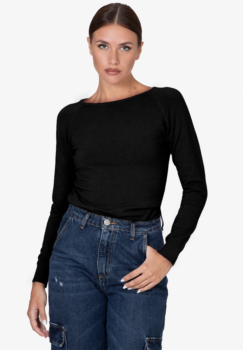 Maglietta nera a maniche lunghe con scollatura ampia, polsini a coste e texture liscia, abbinata a pantaloni in denim blu a vita alta con tasche cargo.