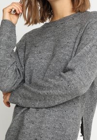 Maglione grigio a maglia con vestibilità rilassata, caratterizzato da un colletto a girocollo, maniche lunghe e spacchi laterali. La texture presenta delle sfumature in tutto il tessuto.