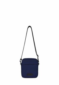 Borsa a tracolla in tessuto blu navy con superficie testurizzata, tracolla nera regolabile, tasca frontale con zip e patch con logo nella parte inferiore. Forma rettangolare.