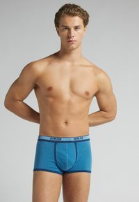 Blaue Boxer-Briefs mit einem marineblauen Bund, auf dem der Text "IUMAN" steht. Der Stoff wirkt glatt und dehnbar und sitzt eng.