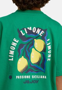 Groene katoenen t-shirt met een grafisch ontwerp van gele citroenen en blauwe accenten. De tekst luidt "LIMONE" en "PASSIONE SICILIANA."