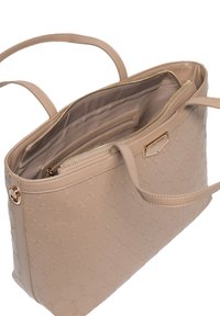 Beige shopper taske med prægede logo mønster, blødt kunstlædermateriale, to håndtag og en lynlåslomme indeni. Guldtonede metaldetaljer.