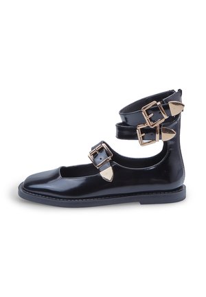 Zapato de charol negro con tacón bajo, que presenta una punta cuadrada y dobles tirantes tobilleros sujetos por hebillas en tono dorado.