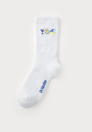 White cotton sock featuring embroidered designs of a cocktail, sun, and lemons in yellow and blue. "On Vacation" is printed in blue.