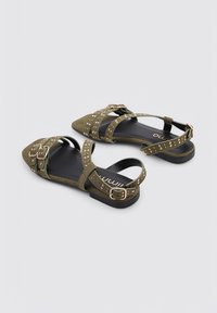 Sandalias verde oliva con suela plana, punta afilada y correas con tachuelas. Cuenta con hebillas ajustables y una suave textura de ante.