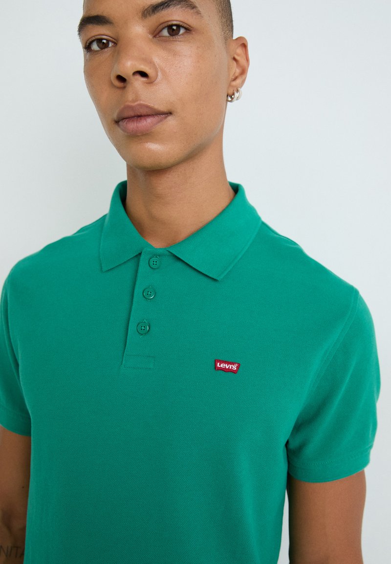 Polo verde in cotone testurizzato, con colletto classico, patta con tre bottoni e logo rosso Levi's sul petto a sinistra.