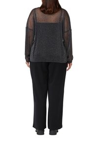 Schwarze Hosen mit weitem Bein, kombiniert mit einem durchsichtigen, funkelnden, dunklen Oberteil mit langen Ärmeln und lockerer Passform, von hinten gezeigt.