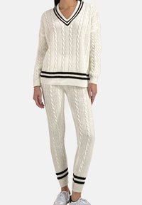Pull crème en maille torsadée avec accents de rayures noires, assorti d'un pantalon en maille torsadée. Comprend un col en V et des poignets ajustés.