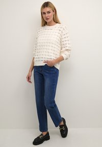 Maglione lavorato a maglia crema con un motivo texturizzato, colletto rotondo e polsini a coste, abbinato a jeans dritti blu chiaro e mocassini neri.