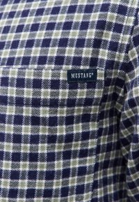 Navy en groen geruite flanellen shirt met een patchzak, met het label "MUSTANG". Zachte textuur en klassiek ruitpatroon.