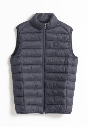 Chaleco acolchado sin mangas en color azul marino, con un alto cuello, cremallera frontal y patrón de costura horizontal. Textura suave, diseño ligero.