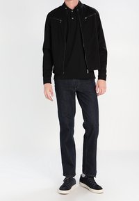 Svart, lättvikts zip-up jacka med ståkrage, två framfickor med dragkedja, ihop med mörkblå jeans och svarta sneakers.