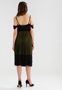 Top nero senza spalline e gonna midi plissè verde oliva con bordino in pizzo nero all'orlo. Tessuto simile alla seta, corpino aderente, silhouette fluida.