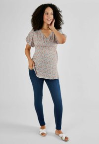 Top cu model floral, cu mâneci scurte tip bufantă și decolteu în V, asociat cu blugi skinny de culoare albastru închis și sandale plate albe. Textură de material neted.