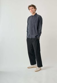 Dunkelgraues Hemd mit Knöpfen und einer Brusttasche, kombiniert mit schwarzen Hosen und hellen Sneakers. Der Stoff wirkt weich und hat eine lockere Passform.