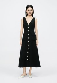 Črna obleka brez rokavov z V-izrezom, dolžine do sredine meč, z teksturirano tkanino, dvema sprednjima žepoma in okrasnimi gumbi.