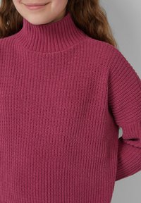 Sweter z golfem wykonany na drutach w głębokim odcieniu różu, z żebrowanym wzorem i luźnym krojem. Widoczne szwy i szerokie mankiety.