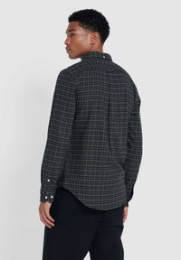 Chemise à boutons en tartan bleu foncé et or, avec un ourlet arrondi et des manches longues, dotée de boutons blancs et d'un détail en boucle à l'arrière.