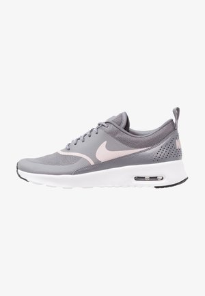 Zapatilla deportiva gris con parte superior de malla, cuello acolchado y mediopie blanca. Presenta el logo de Nike en rosa y amortiguación de aire en el talón.
