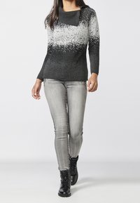 Pull en dégradé noir et gris avec un col châle, en tissu tricoté. Associé à un jean gris clair et des bottines à lacets noires.