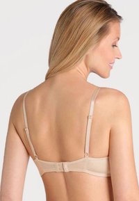 Beige behå med justerbara band och hak-och-öga-stängning. Slät tyg med minimal sömnad, designad för ett sömlöst utseende.