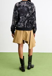 Black and gray tie-dye sweatshirt, contrasting hem, paired with a flowy beige asymmetrical skirt and tall black leather boots.